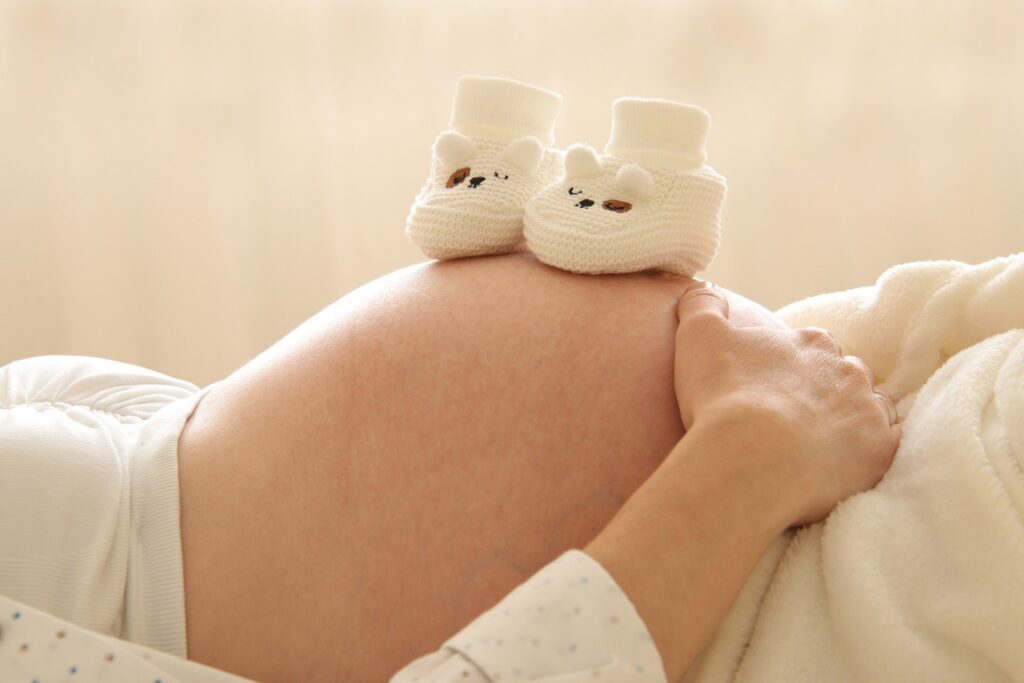 Pregnant woman lying down with baby shoes balancing on her stomach